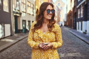 Smiling woman wearing sunglasses exploring city streets with her cellphone